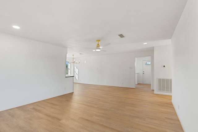 empty room featuring ceiling fan with notable chandelier and light wood-type flooring