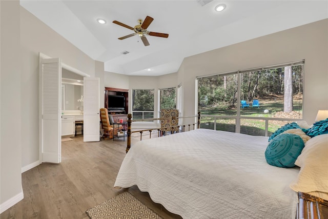 bedroom featuring ceiling fan, light hardwood / wood-style floors, vaulted ceiling, and ensuite bath