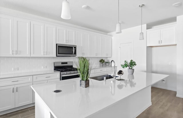 kitchen with white cabinets, appliances with stainless steel finishes, pendant lighting, and an island with sink