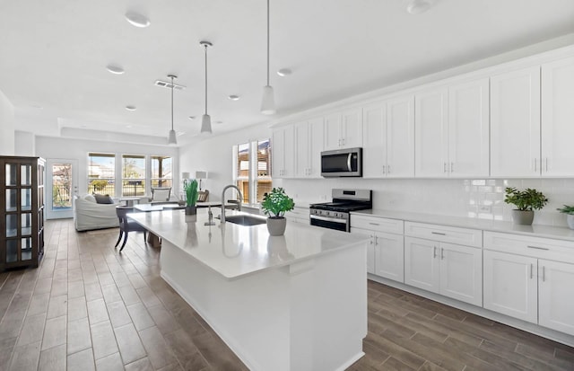 kitchen featuring white cabinets, appliances with stainless steel finishes, decorative light fixtures, and a center island with sink