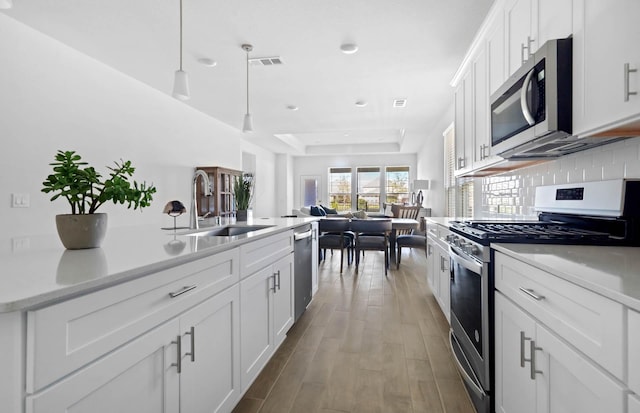 kitchen with white cabinets, a raised ceiling, sink, decorative light fixtures, and stainless steel appliances