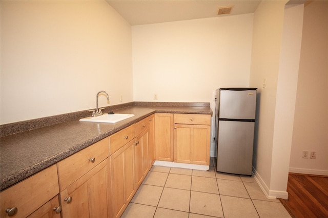 kitchen featuring light brown cabinetry, light tile patterned floors, sink, and stainless steel refrigerator