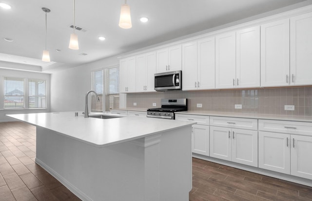 kitchen with appliances with stainless steel finishes, white cabinetry, hanging light fixtures, and a kitchen island with sink