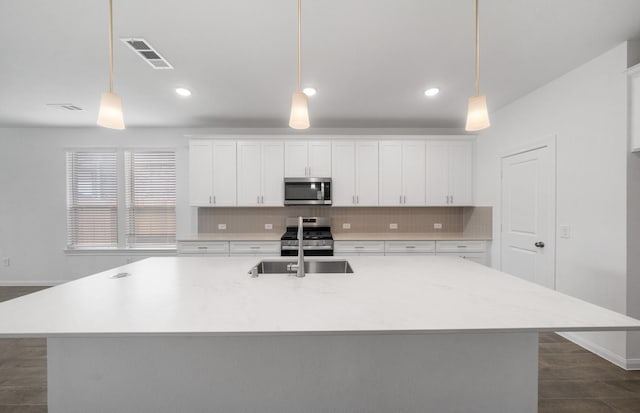 kitchen with an island with sink, stainless steel appliances, and decorative light fixtures