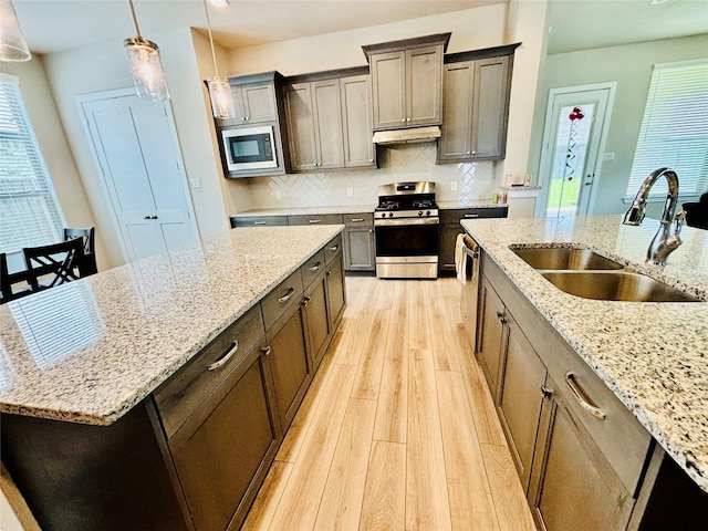 kitchen with light stone countertops, sink, stainless steel appliances, tasteful backsplash, and decorative light fixtures