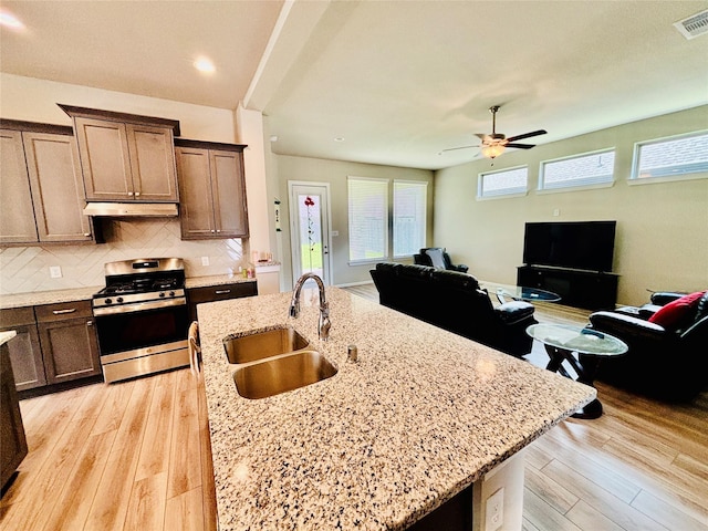 kitchen featuring ceiling fan, sink, tasteful backsplash, light stone counters, and stainless steel range oven