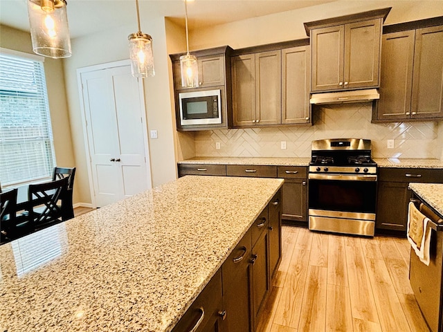 kitchen with light stone counters, decorative backsplash, pendant lighting, and stainless steel range oven