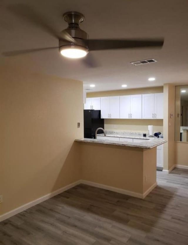 kitchen with kitchen peninsula, black refrigerator, white cabinets, and dark hardwood / wood-style flooring