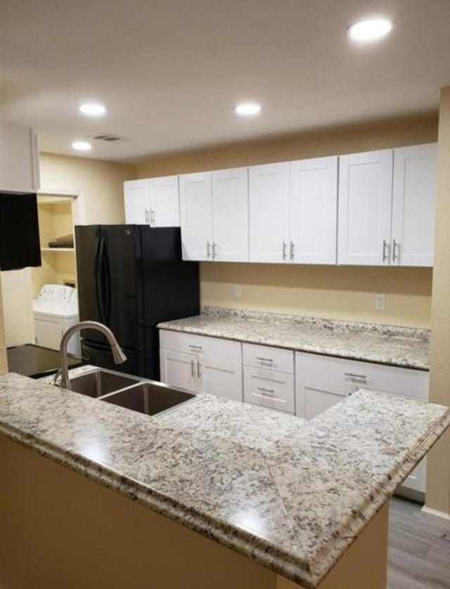 kitchen with washing machine and clothes dryer, black refrigerator, and white cabinets