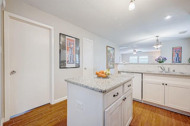 kitchen with pendant lighting, dishwasher, sink, a kitchen island, and white cabinetry