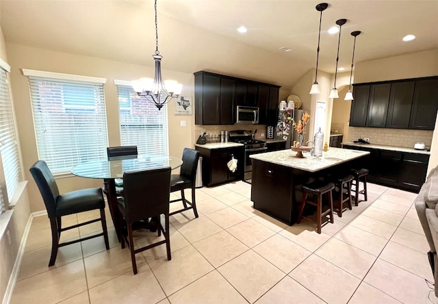 kitchen with a kitchen island with sink, light tile patterned floors, pendant lighting, and appliances with stainless steel finishes