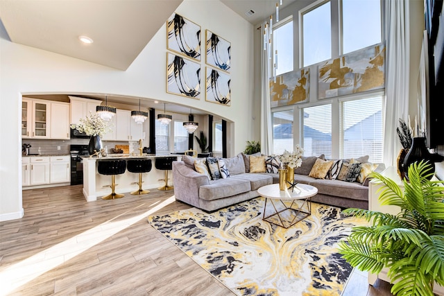 living room featuring a high ceiling, light wood-type flooring, and an inviting chandelier