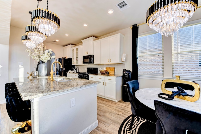 kitchen featuring white cabinetry, a notable chandelier, pendant lighting, a center island with sink, and black appliances