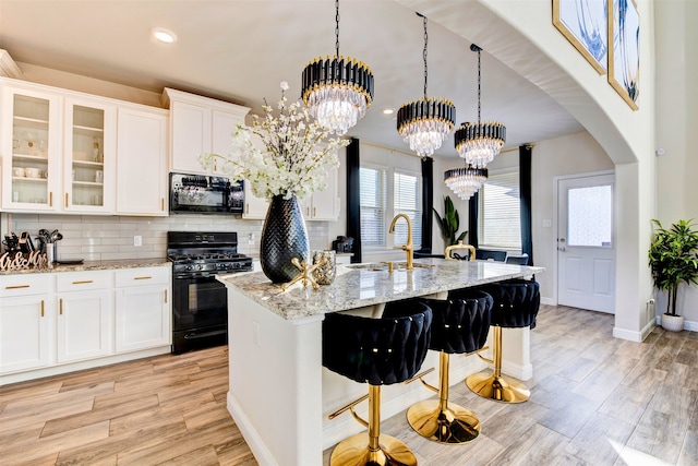 kitchen with sink, an island with sink, a chandelier, white cabinets, and black appliances