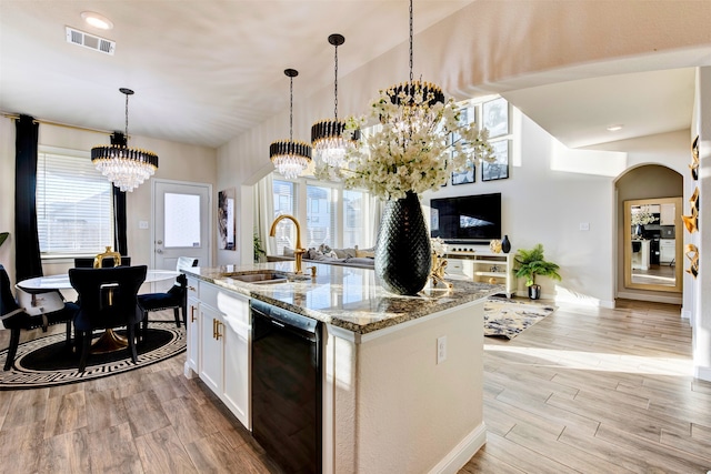 kitchen featuring a kitchen island with sink, black dishwasher, light stone counters, and a notable chandelier