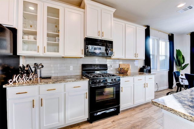 kitchen with decorative backsplash, light wood-type flooring, light stone counters, black appliances, and white cabinetry