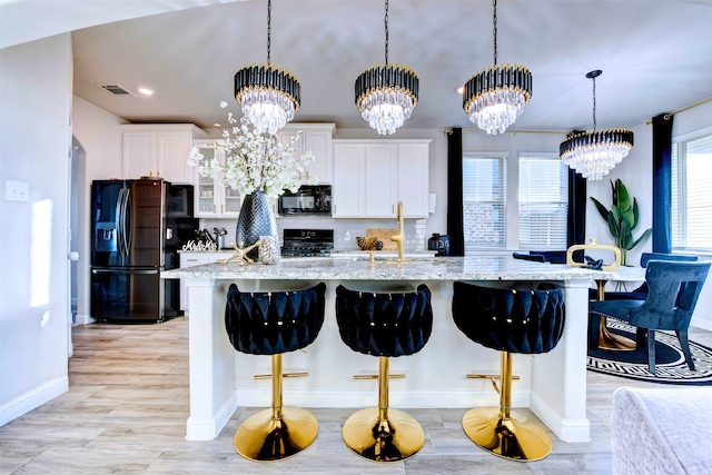 kitchen featuring sink, an inviting chandelier, a kitchen bar, white cabinets, and black appliances