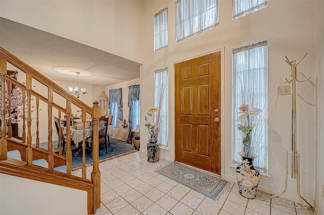 tiled foyer entrance featuring a healthy amount of sunlight, a towering ceiling, and a chandelier