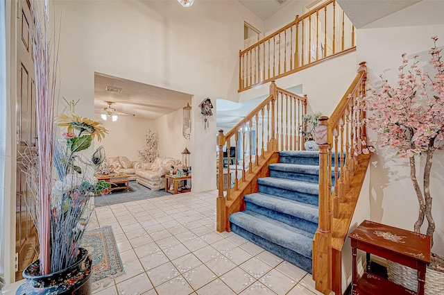 stairs with tile patterned floors, ceiling fan, and a towering ceiling