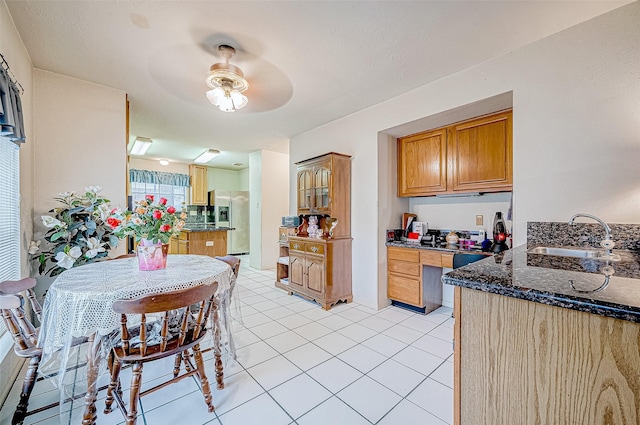 kitchen featuring dark stone counters, sink, ceiling fan, light tile patterned flooring, and stainless steel fridge with ice dispenser