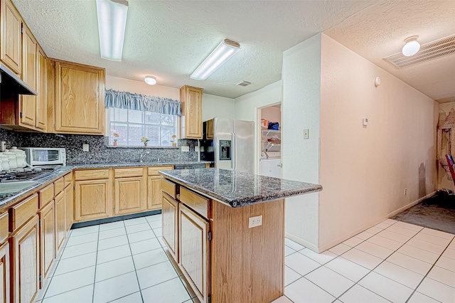 kitchen with tasteful backsplash, dark stone counters, light tile patterned floors, stainless steel fridge with ice dispenser, and a kitchen island