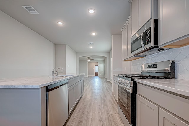 kitchen with backsplash, sink, light hardwood / wood-style flooring, ceiling fan, and stainless steel appliances