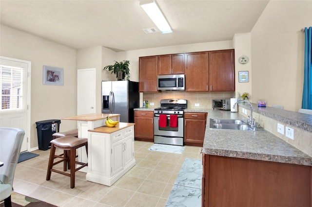 kitchen with sink, stainless steel appliances, tasteful backsplash, a breakfast bar, and light tile patterned floors