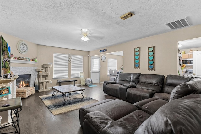 living room with ceiling fan, dark wood-type flooring, a textured ceiling, and a brick fireplace