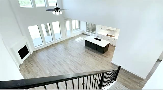 unfurnished living room with a healthy amount of sunlight, ceiling fan, light hardwood / wood-style floors, and a high ceiling