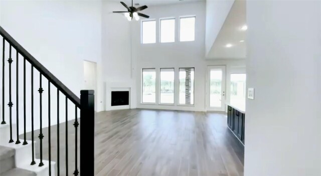 unfurnished living room featuring a towering ceiling, ceiling fan, and light hardwood / wood-style flooring