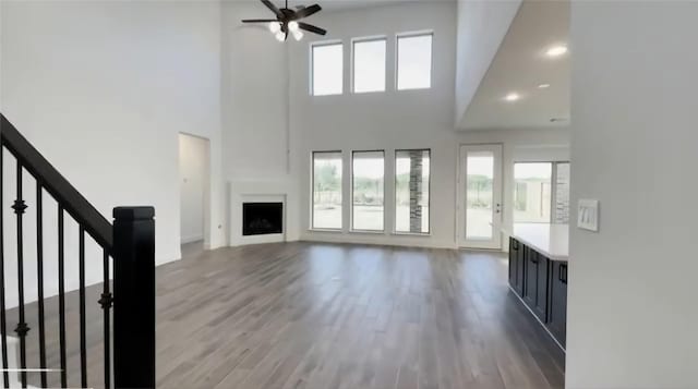 unfurnished living room featuring ceiling fan, light hardwood / wood-style flooring, a towering ceiling, and a large fireplace