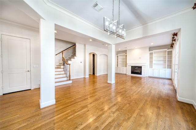 unfurnished living room featuring light hardwood / wood-style floors, built in features, crown molding, and an inviting chandelier