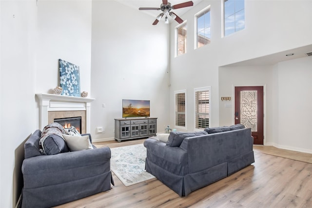 living room with ceiling fan, a fireplace, a towering ceiling, and light hardwood / wood-style flooring