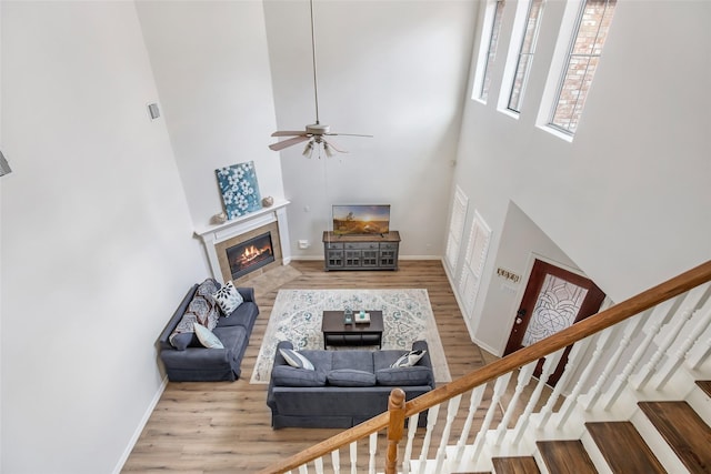 living room with ceiling fan, a towering ceiling, and light hardwood / wood-style floors