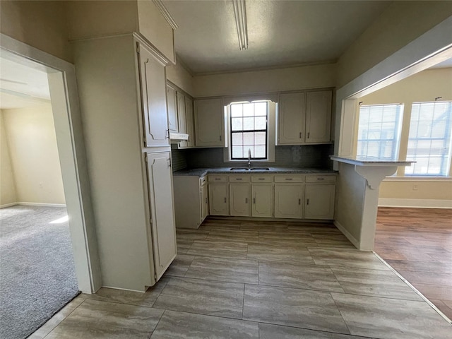 kitchen featuring sink, tasteful backsplash, kitchen peninsula, light colored carpet, and a breakfast bar