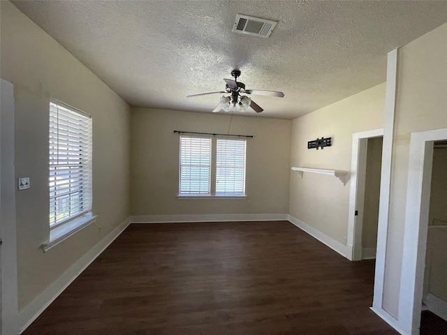 empty room with a textured ceiling, dark hardwood / wood-style floors, ceiling fan, and a healthy amount of sunlight