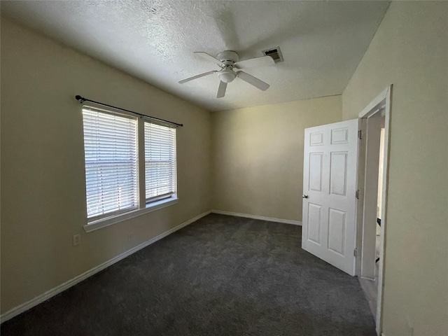 spare room featuring ceiling fan, dark carpet, and a textured ceiling