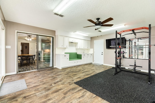 workout room featuring ceiling fan, wood-type flooring, and a textured ceiling