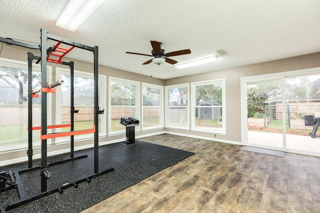 workout room with ceiling fan, wood-type flooring, and a textured ceiling