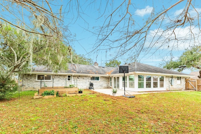 rear view of property featuring a sunroom, a patio area, and a lawn