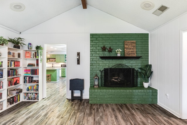 living room featuring hardwood / wood-style flooring, lofted ceiling with beams, a textured ceiling, and a brick fireplace