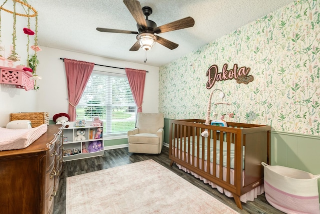 bedroom featuring a textured ceiling, ceiling fan, dark wood-type flooring, and a nursery area