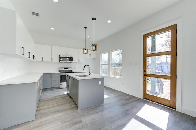 kitchen featuring sink, gray cabinets, an island with sink, decorative light fixtures, and stainless steel appliances