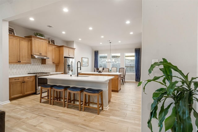 kitchen featuring tasteful backsplash, a kitchen island with sink, hanging light fixtures, and stainless steel appliances