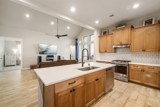 kitchen featuring appliances with stainless steel finishes, light wood-type flooring, backsplash, sink, and an island with sink