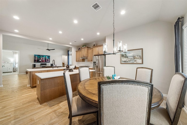 dining area with vaulted ceiling, light hardwood / wood-style flooring, ceiling fan with notable chandelier, and sink