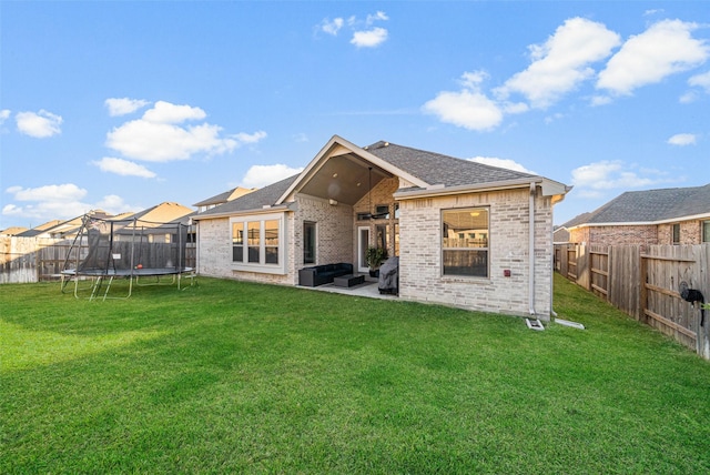 rear view of property featuring a patio, a trampoline, ceiling fan, and a lawn