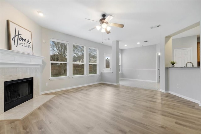 unfurnished living room featuring ceiling fan, light wood-type flooring, and a tiled fireplace