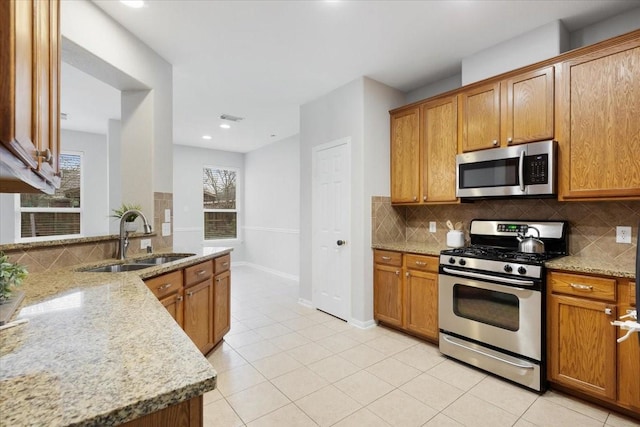 kitchen featuring light stone countertops, appliances with stainless steel finishes, backsplash, sink, and light tile patterned flooring