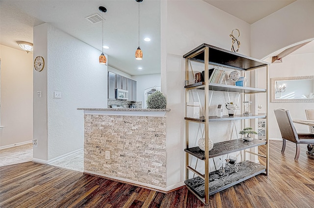 interior space featuring light stone counters, backsplash, kitchen peninsula, hardwood / wood-style floors, and decorative light fixtures